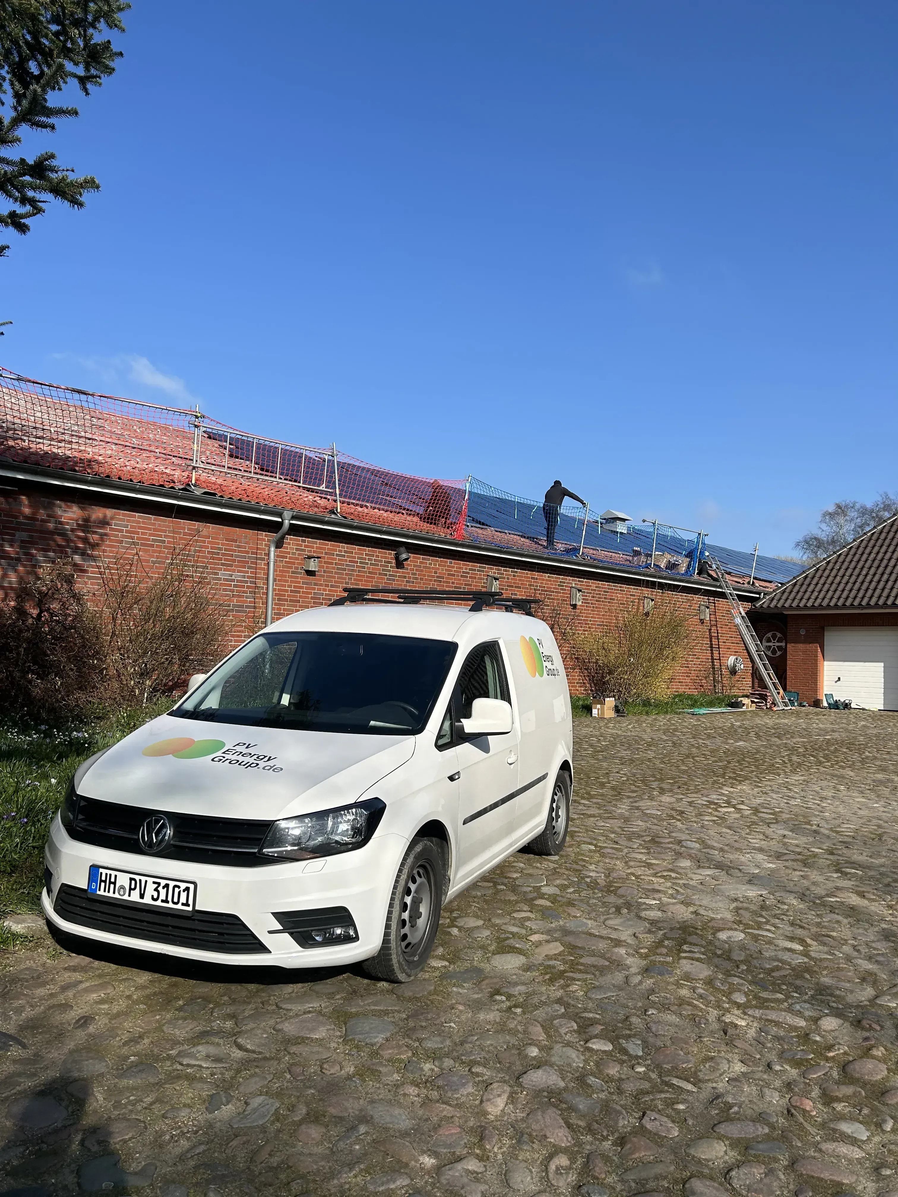 Firmenwagen vor Wohnhaus mit Solaranlagen-Montage auf dem Dach durch Monteur