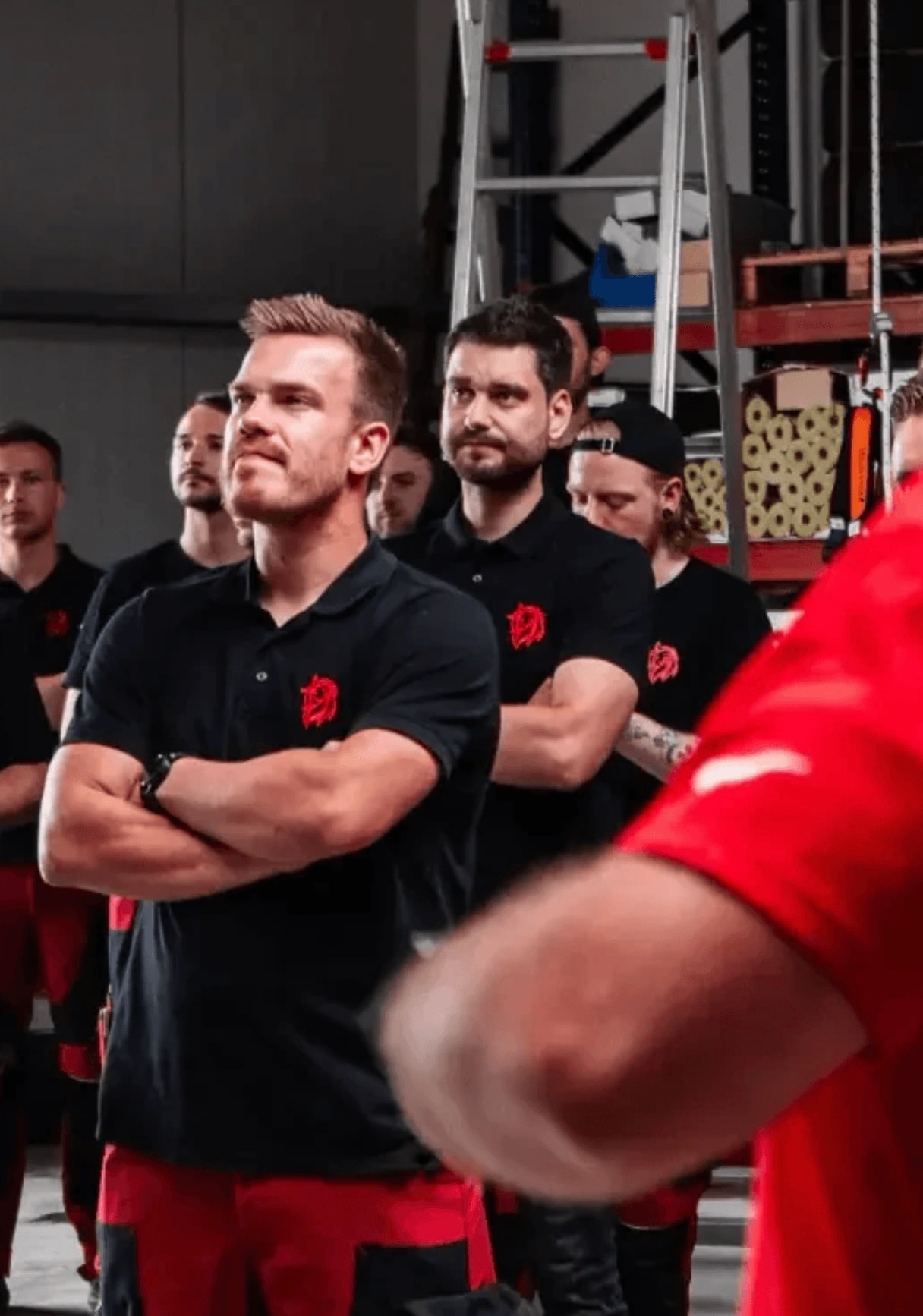 Team in schwarzen Poloshirts mit rotem Logo steht in einer Werkstatt